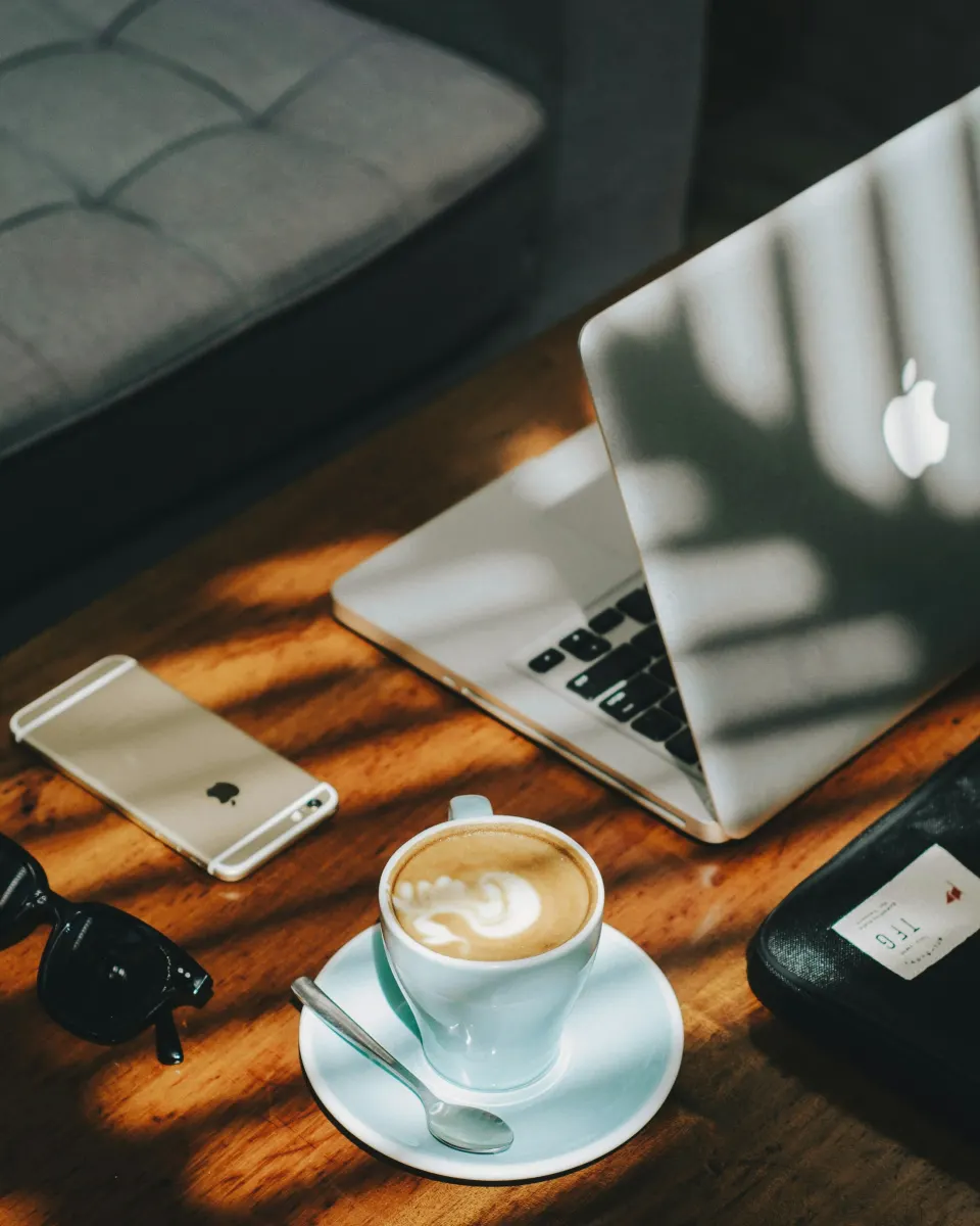 Laptop, phone and coffee on a desk in morning light